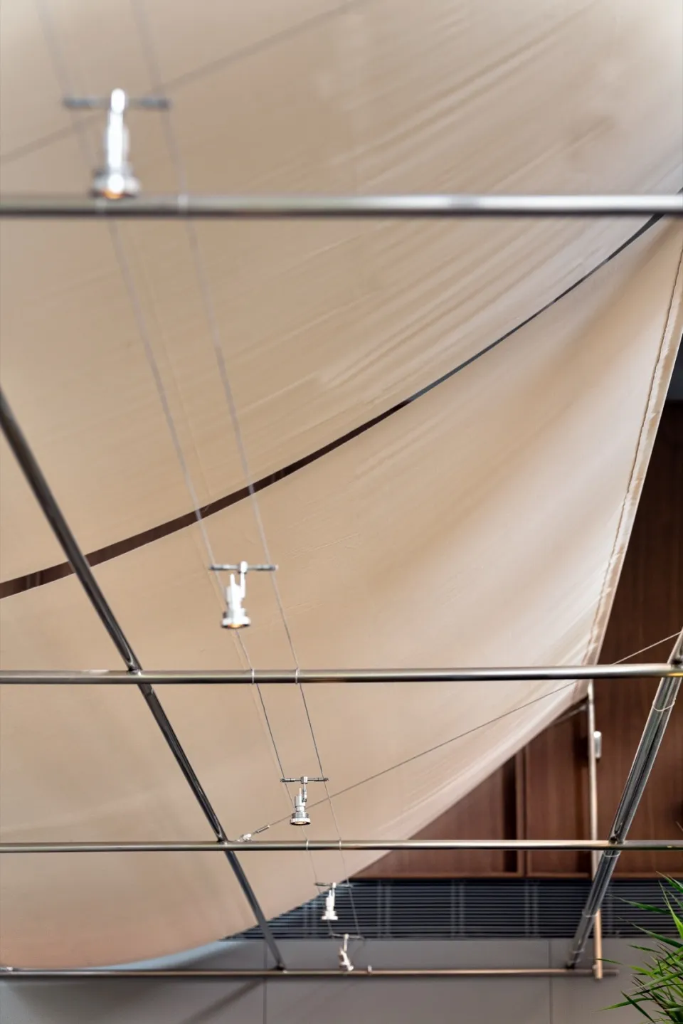 Low-angle view of a modern curved tension fabric ceiling system with chrome track lighting and metal support structure.