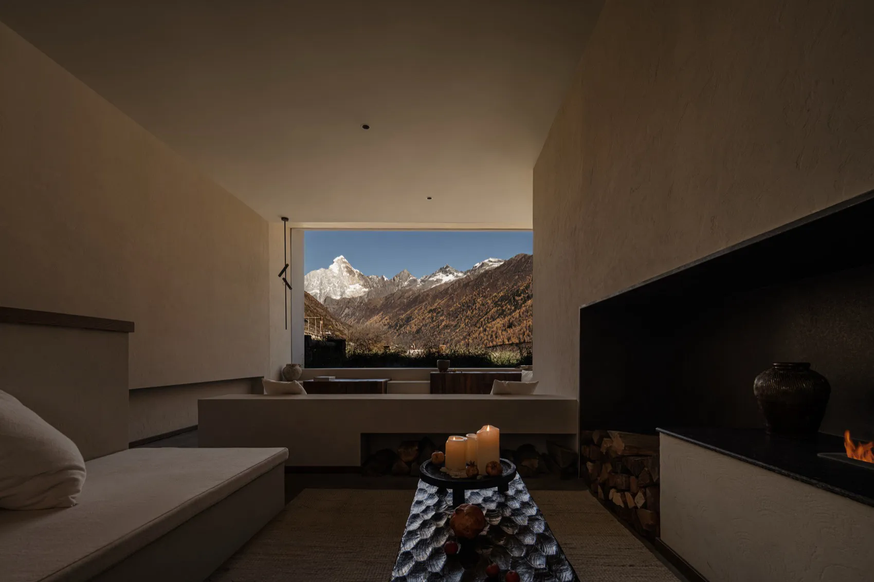 Minimalist bedroom interior with built-in daybed, modern fireplace, textured plaster walls, and large window overlooking snow-capped mountain range.