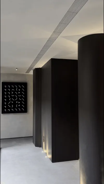 Modern minimalist hallway featuring tall dark wood cabinetry, cylindrical column, light gray microcement floor, and black abstract bird artwork on the wall.