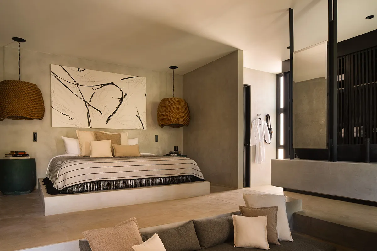 Modern minimalist bedroom featuring a low platform bed with black and white striped bedding, large abstract ink painting, two oversized woven rope pendant lights, and raw concrete walls in neutral earth tones.