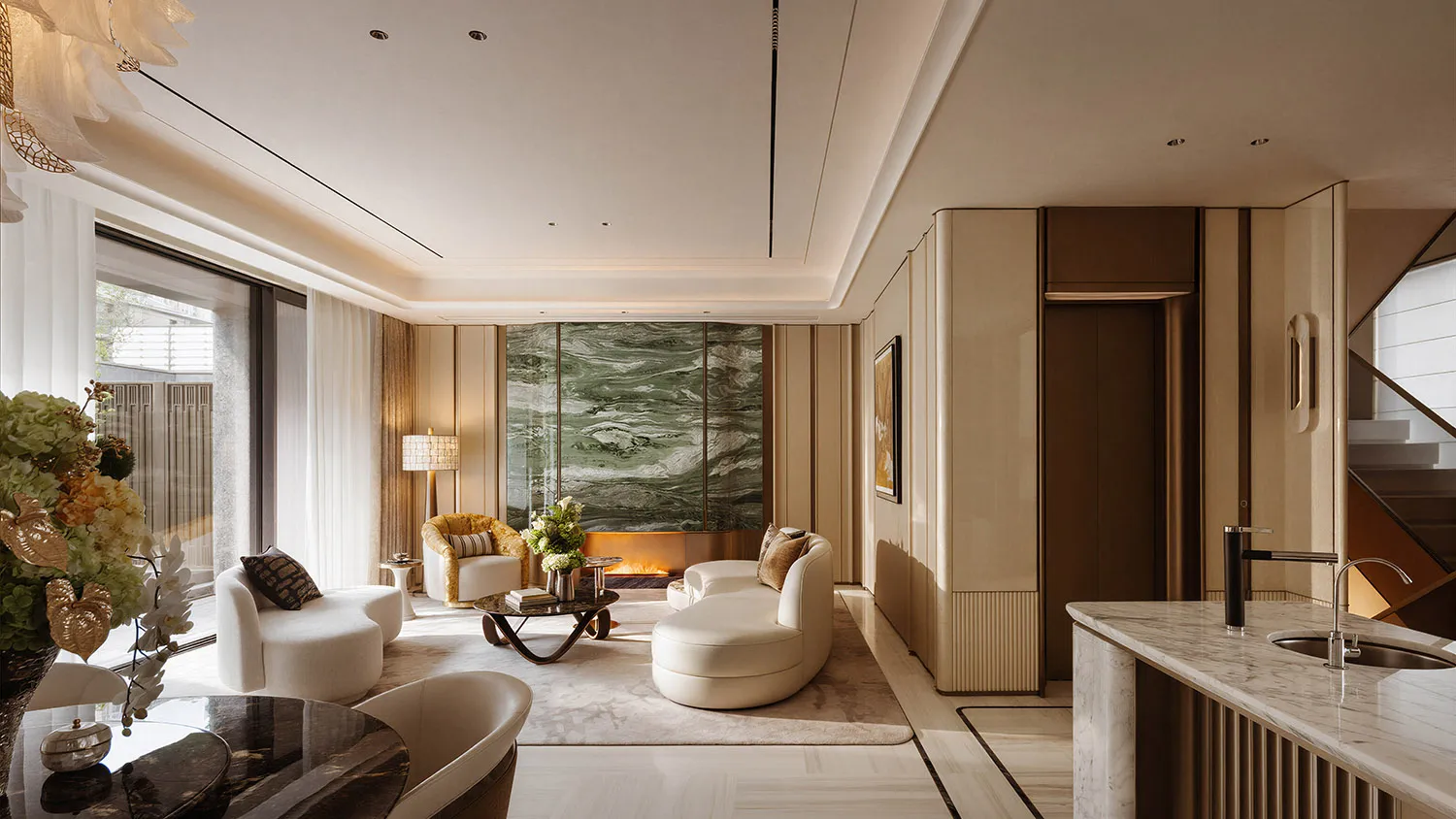 Modern luxury living room with a striking green marble feature wall, curved white sofas, marble kitchen island, and warm ambient lighting.