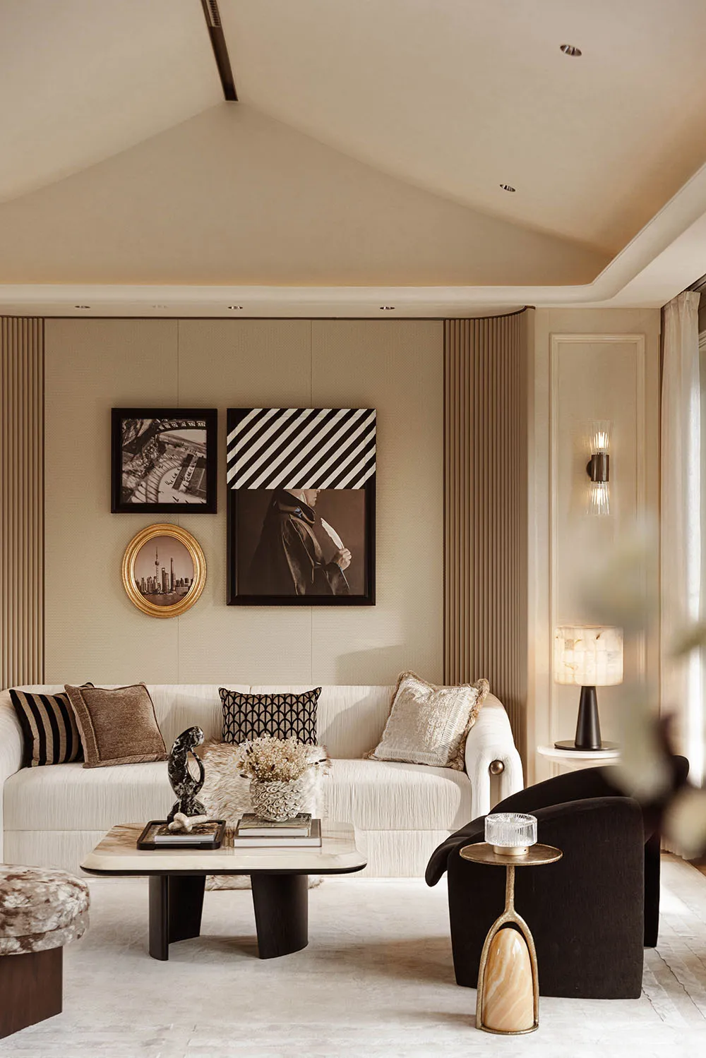 Modern neutral living room with a white curved sofa, dark velvet armchair, marble coffee table, and a gallery wall displaying black and white photography and a gold-framed Shanghai skyline portrait.