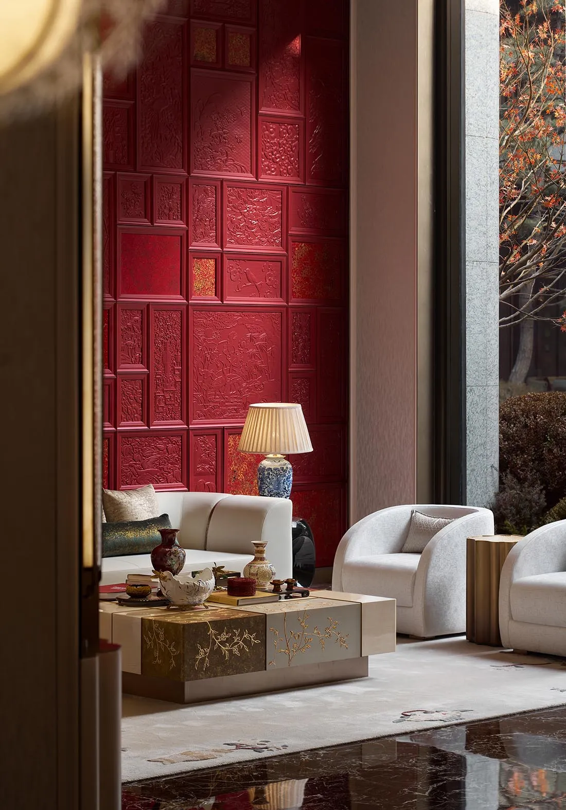 Modern living room featuring a dramatic red lacquered wall with intricate traditional Chinese carvings, paired with white curved sofas and a low coffee table with gold detailing.
