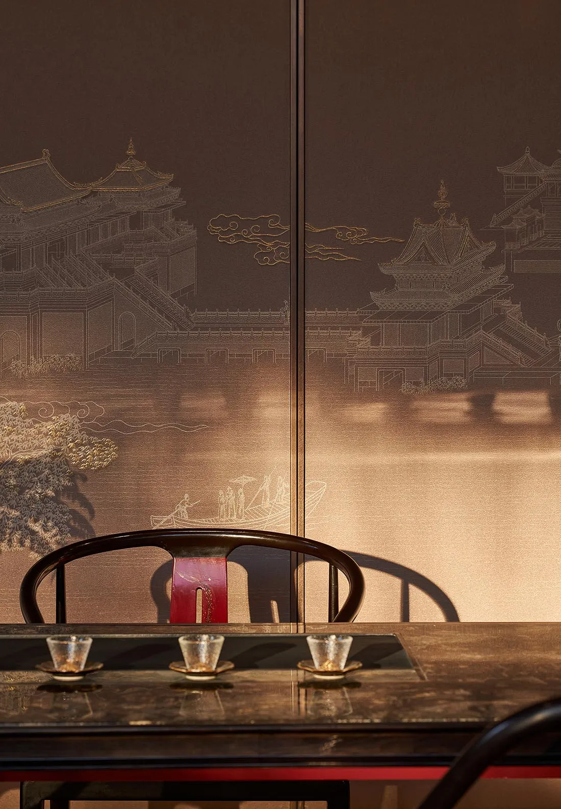 Dark rosewood horseshoe-back chair in front of a luxurious dark brown embroidered Chinese landscape screen featuring pavilions, mountains and river scenes, with three tea cups on a lacquered table.