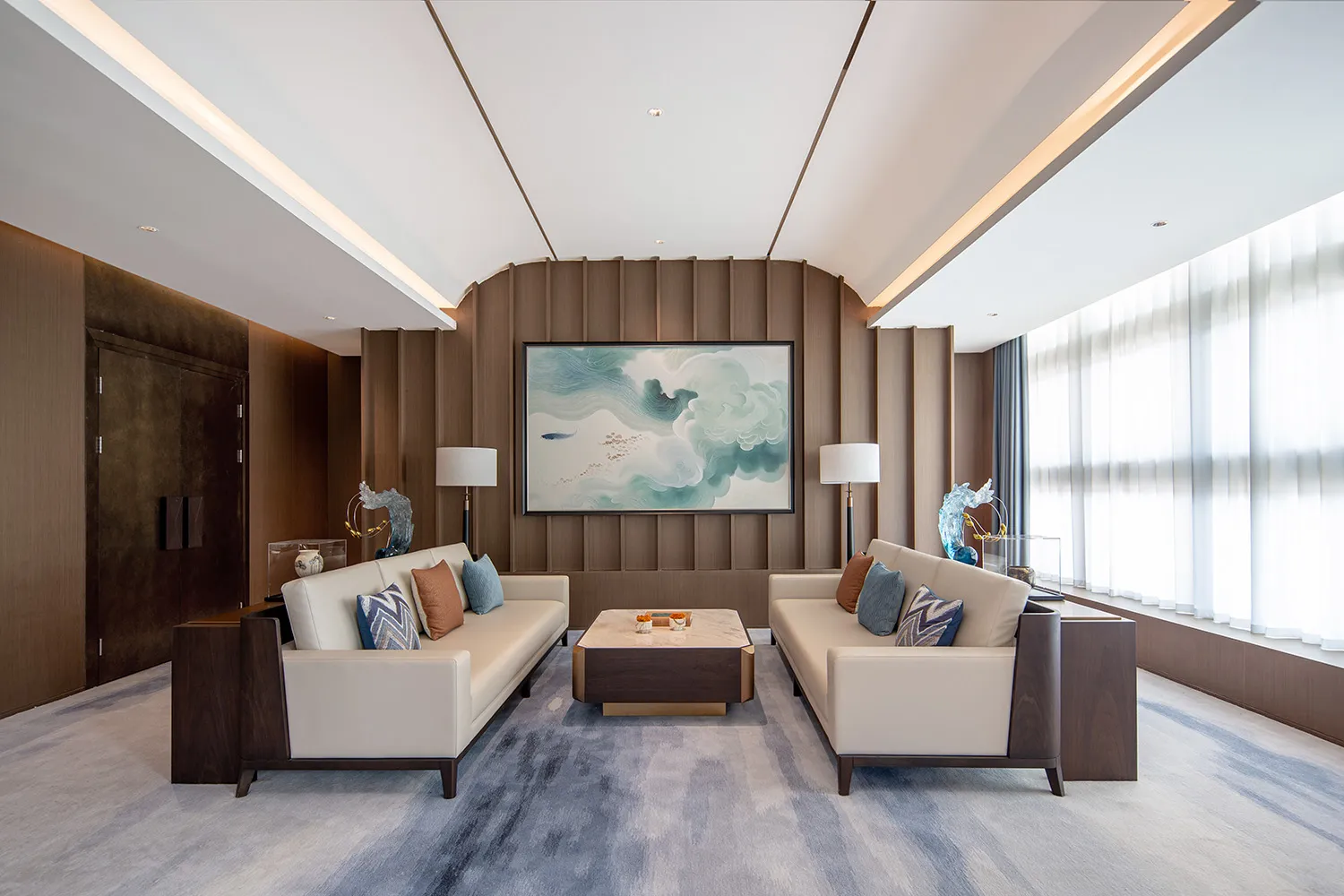 Modern Chinese living room with two cream sofas facing each other, a curved walnut wood feature wall, large abstract jade landscape painting, marble coffee table, and blue-grey area rug.