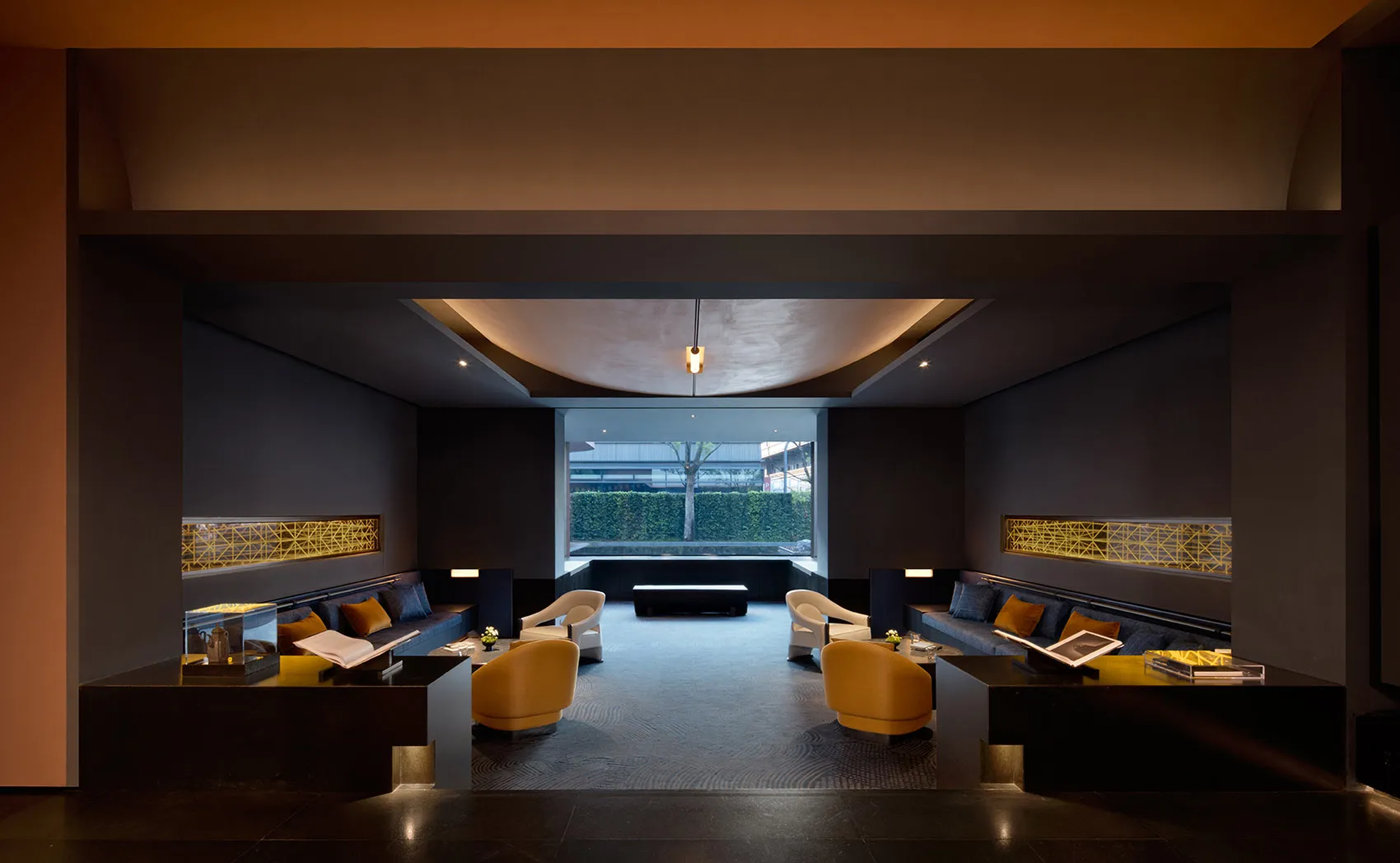 Modern luxury hotel lobby lounge featuring dark stone walls, curved ceiling, mustard yellow swivel chairs, deep blue sofas, and golden lattice light fixtures.