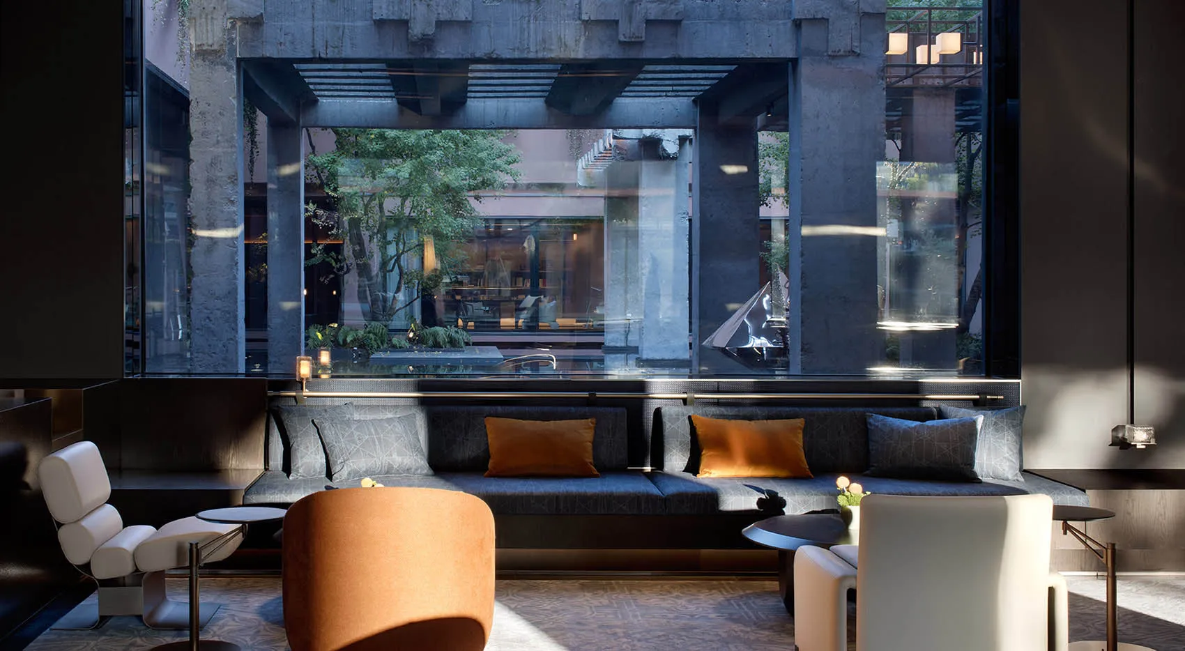Modern lounge with dark concrete structural beams, large glass walls overlooking a garden, blue-grey sectional sofa with orange accent pillows, and contemporary orange and white lounge chairs.