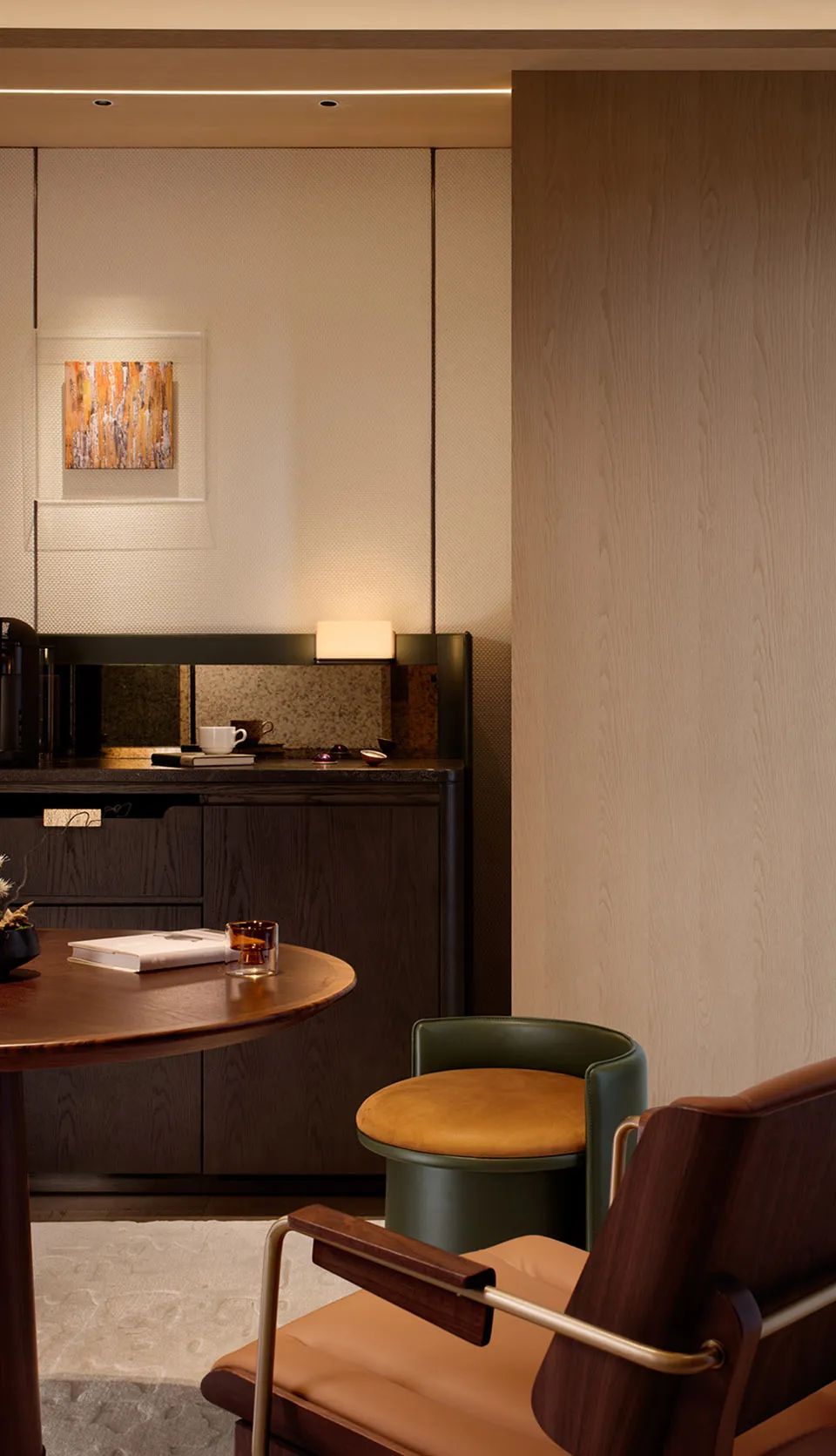 Modern minimalist living room corner with dark walnut storage cabinet, round wooden coffee table, green leather swivel chair with tan cushion, and warm ambient lighting.