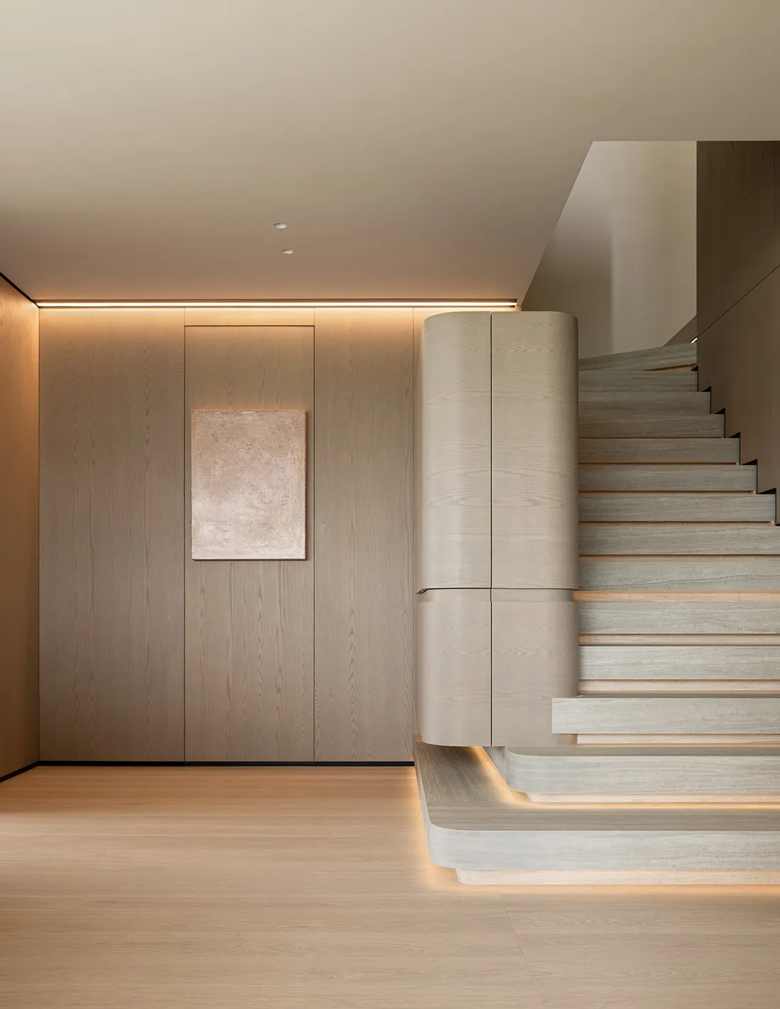Modern minimalist entryway featuring a floating oak staircase with curved balustrade and continuous LED lighting integrated into the treads and ceiling cove.