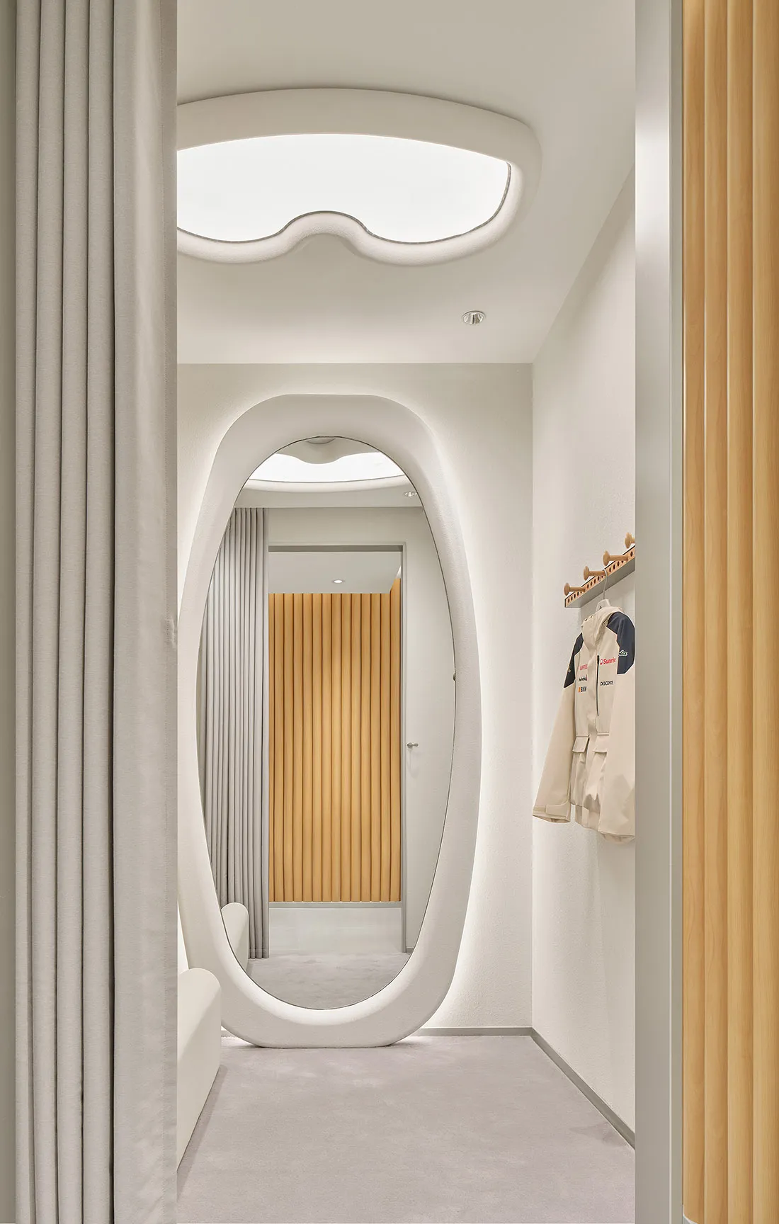 Modern minimalist hallway with white organic-shaped arched doorway, light oak wood paneling, and soft neutral textiles.