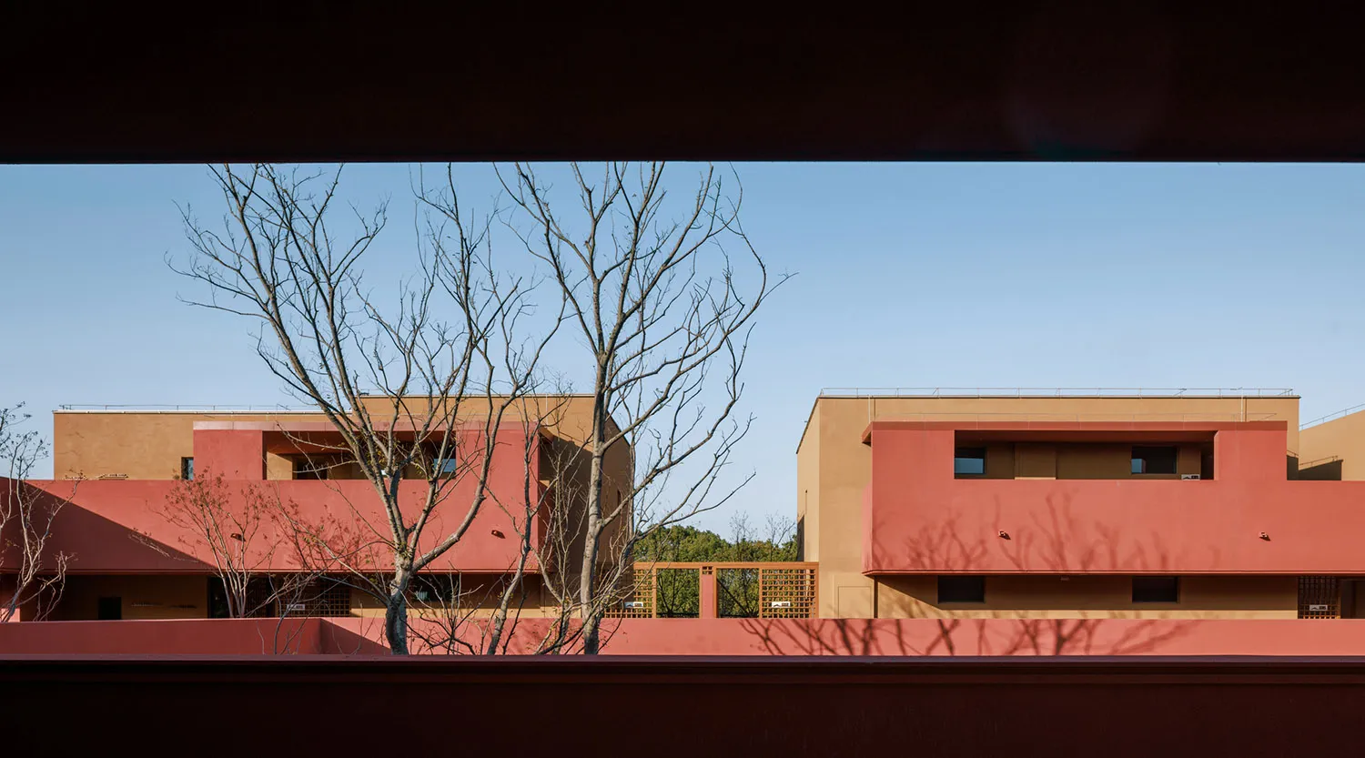 Modern residential buildings with terracotta and beige stucco facades, bare trees in foreground under a clear blue sky.