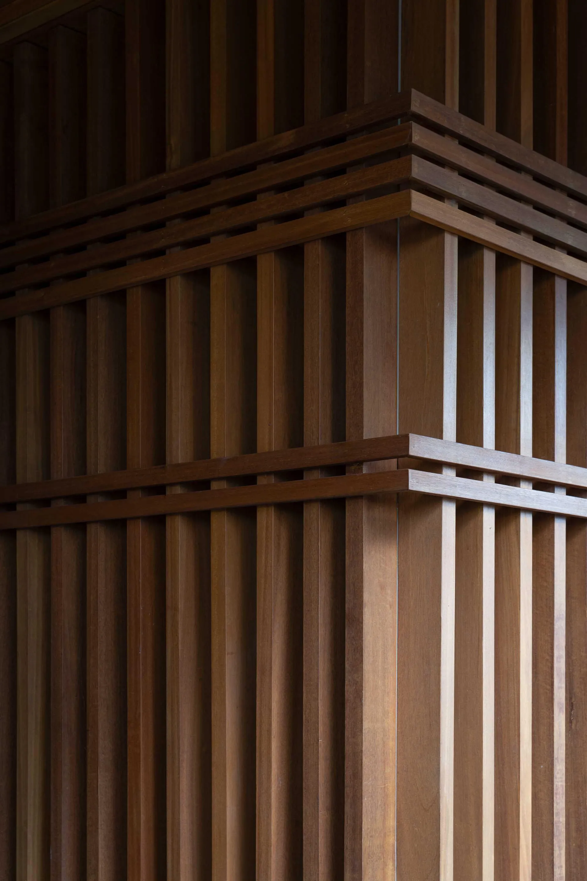 Close-up of a warm brown teak wood wall featuring vertical slats intersected by thick horizontal beams and decorative wood framing.