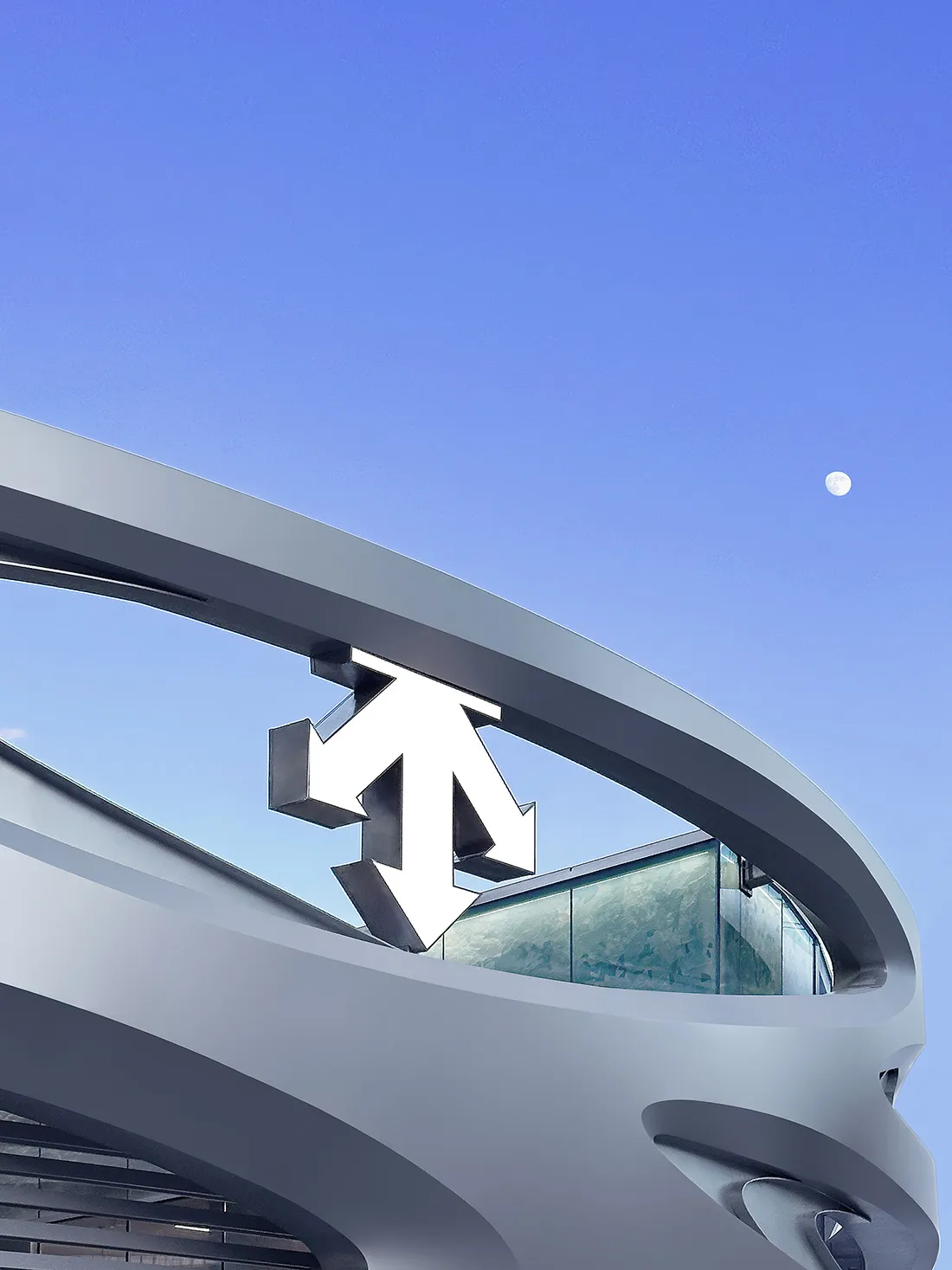 Low angle view of a modern curved metallic building facade featuring a large white and black three-dimensional arrow sculpture against a clear blue evening sky with a visible moon.