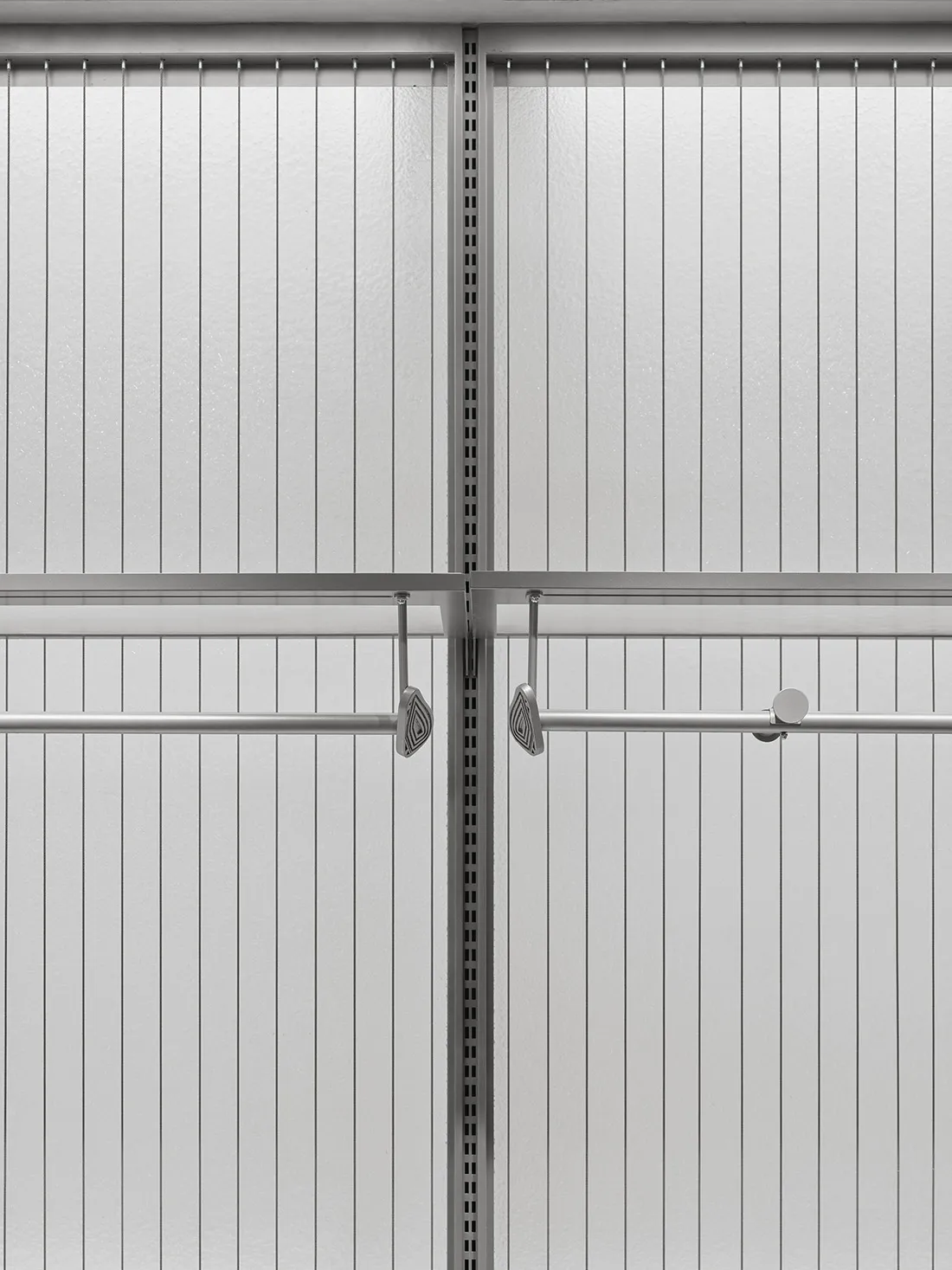 Close-up view of a minimalist white closet interior featuring vertical fluted panels, adjustable stainless steel hanging rods, and decorative metal hooks.