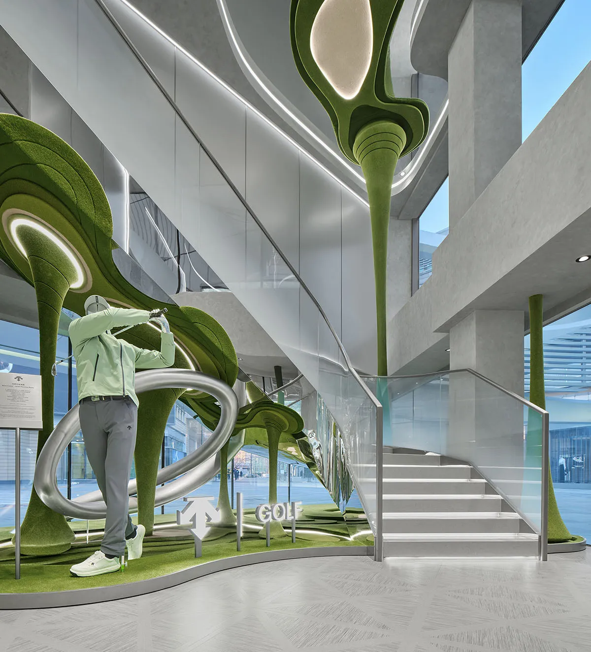 Man swinging golf club inside a modern retail space featuring large organic green felt sculptures, dramatic lighting, and a glass staircase.