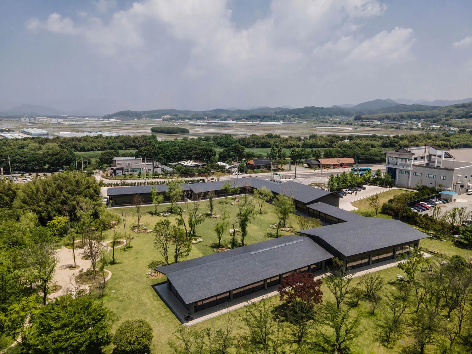 Aerial photograph of a modern cultural center in Yilan, Taiwan, featuring long dark-roofed buildings arranged in an L-shape, surrounded by green lawns, trees, and rural landscape with mountains in the background.