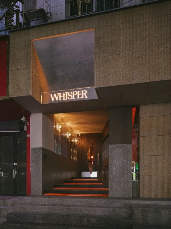 Night view of modern restaurant entrance named Whisper with glowing steps, textured concrete walls, and warm ambient lighting.