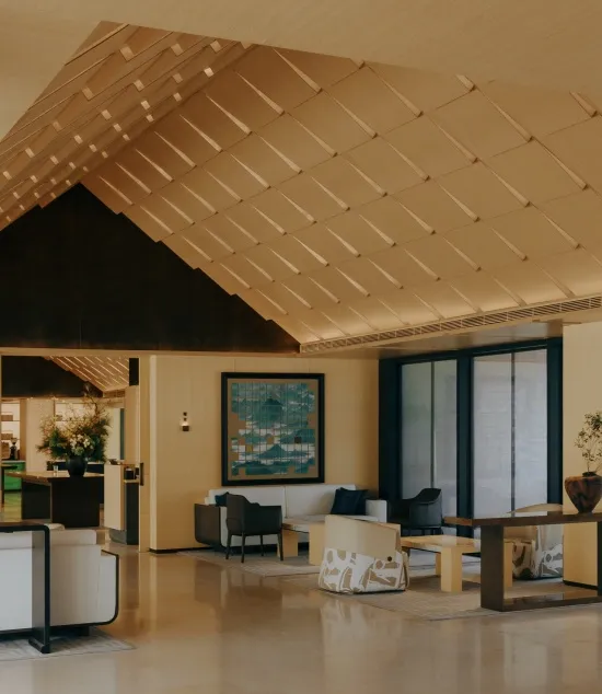Modern hotel lobby featuring a dramatic angled wooden coffered ceiling, minimalist seating, large abstract art, and polished stone floors.