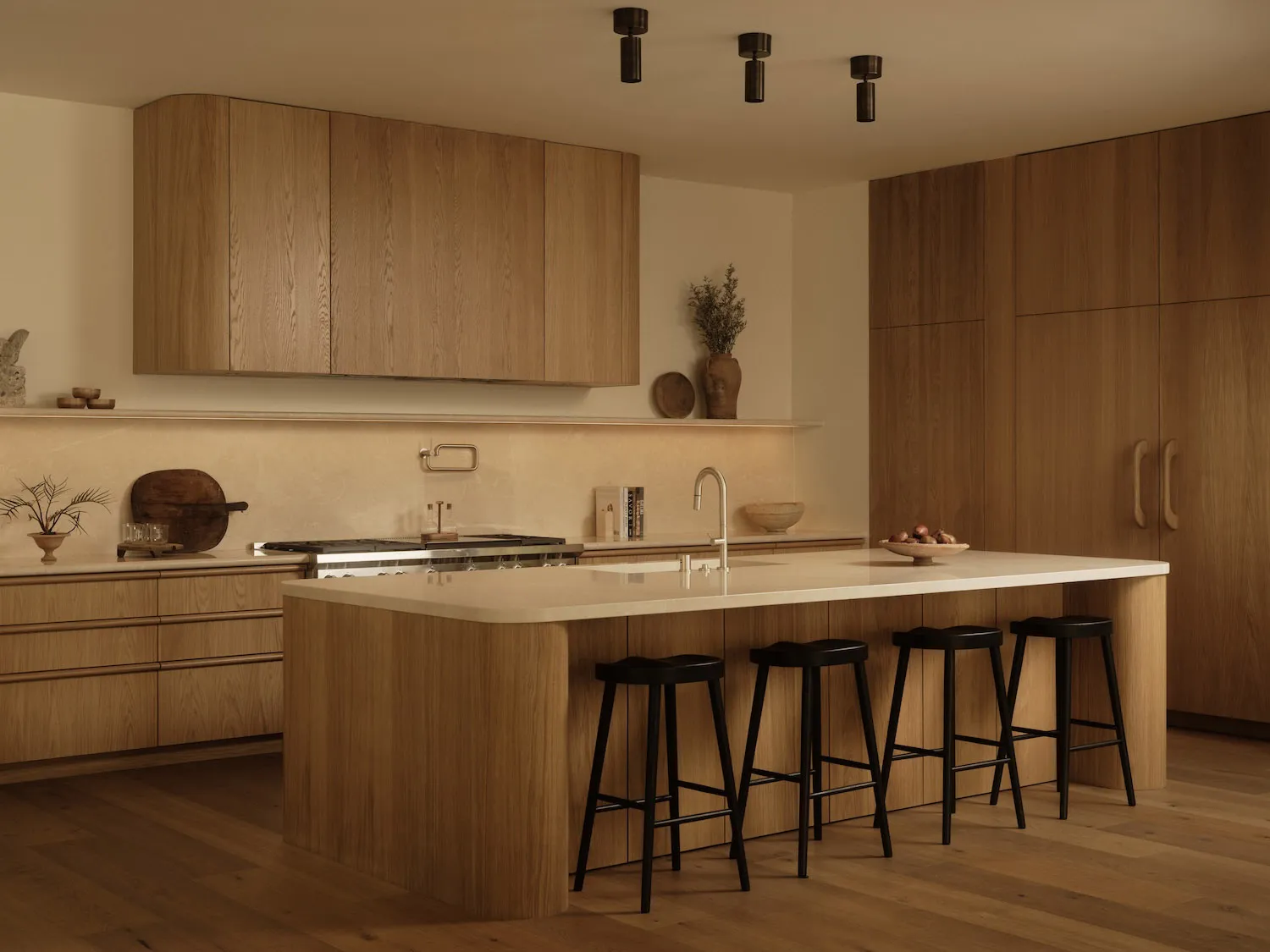 Modern minimalist kitchen featuring light oak cabinetry, a large white quartz kitchen island with black stools, and warm ambient lighting.
