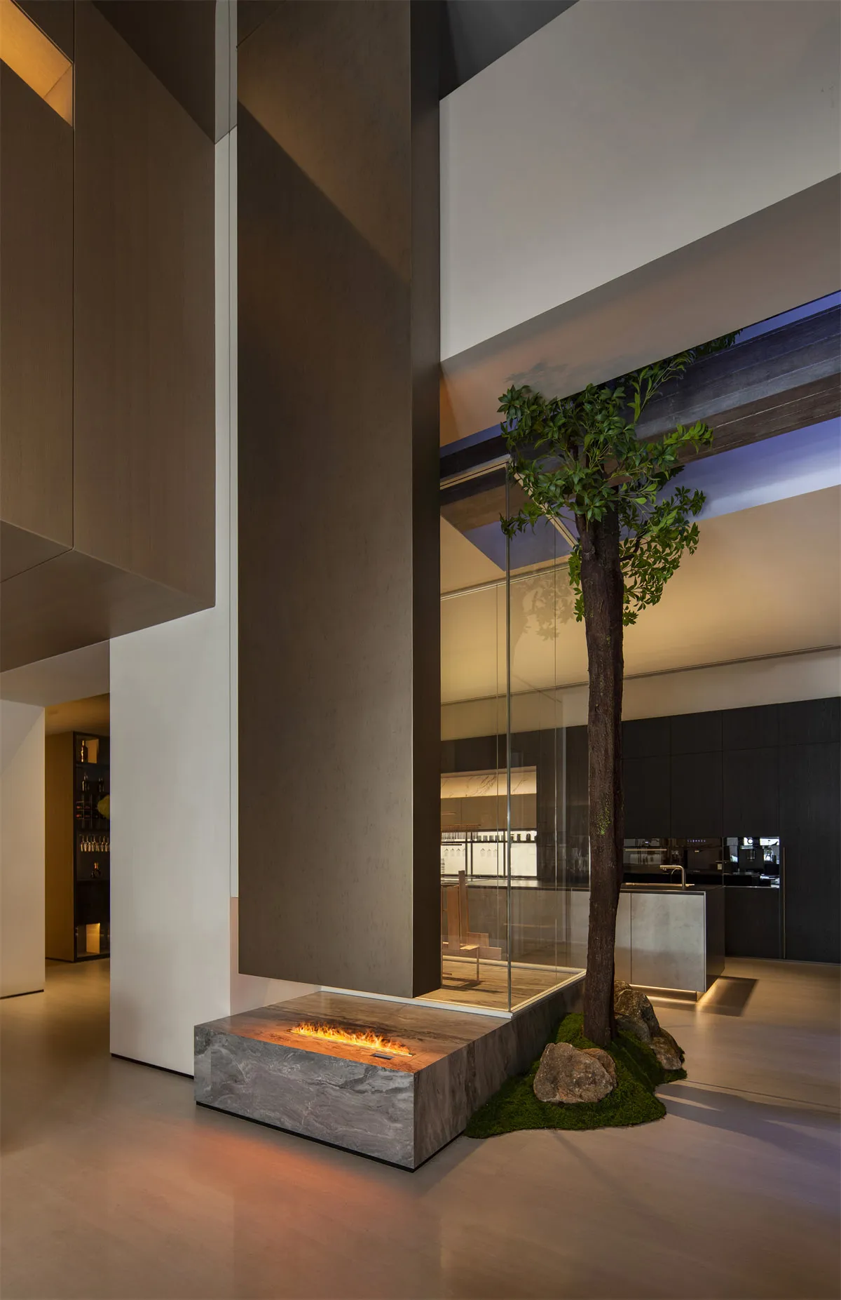 Modern minimalist living room with a tall indoor tree growing beside a stone platform linear fireplace, micro-cement walls, and warm ambient lighting.