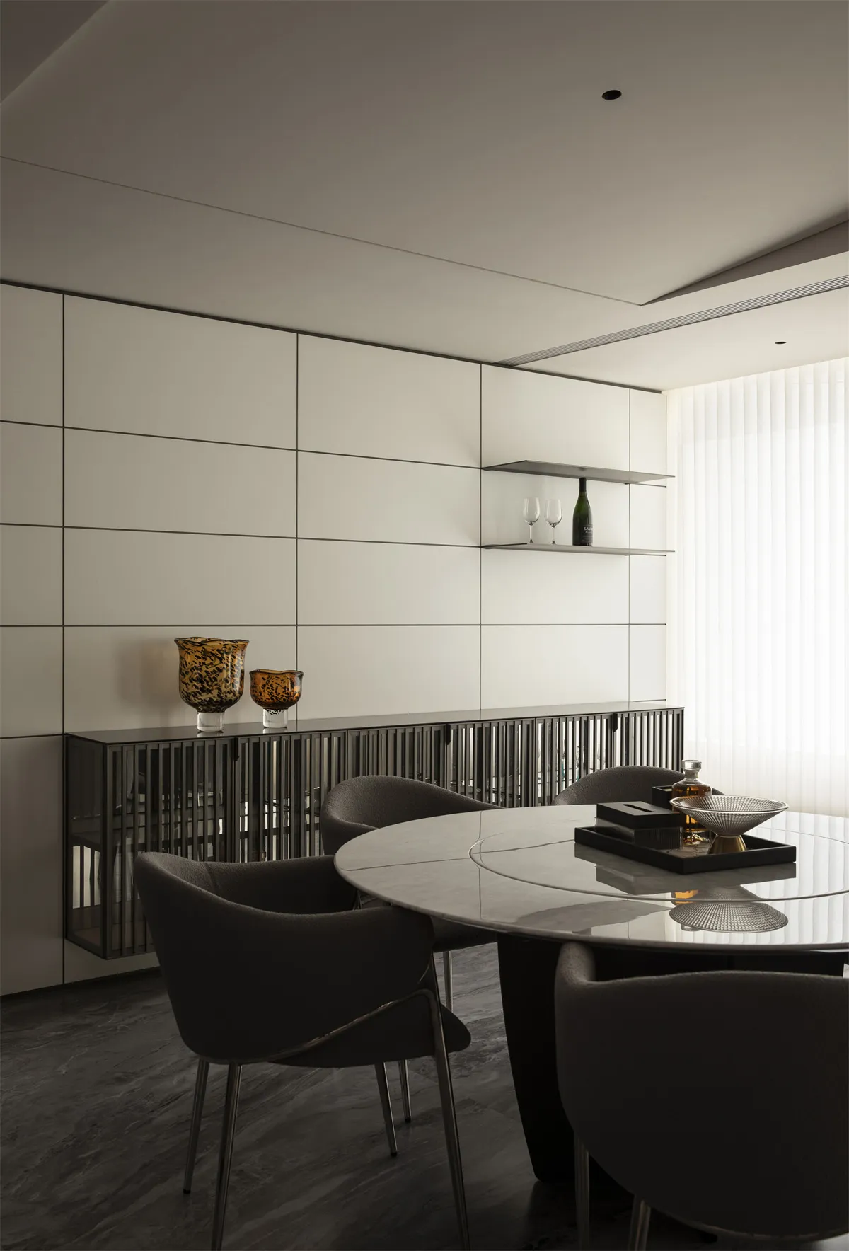 Modern minimalist dining room featuring a round marble dining table, dark upholstered dining chairs, and a black metal slatted sideboard against a white grid wall.