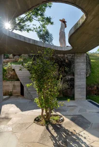 A minimalist outdoor space featuring a concrete archway, stairs, and a tree in a circular patio.