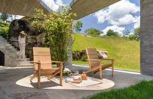 Two wooden Adirondack chairs on a sunny day with concrete walls and a grassy hill in the background.