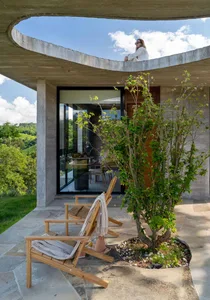 A modern residential home with a concrete exterior, featuring a balcony overlooking green hills.