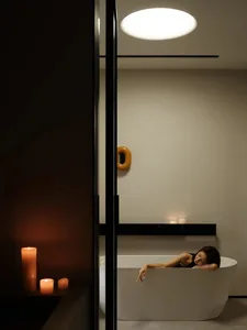 A minimalist bathroom scene with a white porcelain bathtub, candles, and a circular light fixture on the ceiling.