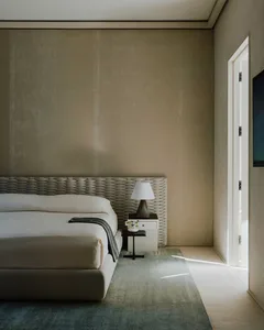 A minimalist bedroom with a bed that has a wicker headboard and a white lamp with a black base on a white nightstand.