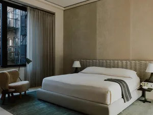A minimalist bedroom featuring neutral textiles and a textured, woven headboard
