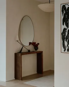A minimalist entrance console table with a round mirror, red flowers, and a candle holder.