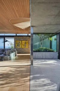 A modern interior living room with concrete walls, wood ceiling, and large windows.