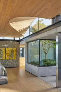 Modern living room featuring large glass windows with a view of a garden, a stone accent wall, and a grey sofa on a wooden fl