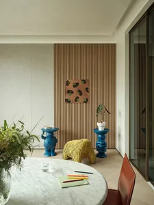 A modern living room featuring a round marble table with colored pencils and a notebook, a yellow furry pouf, and blue bear s