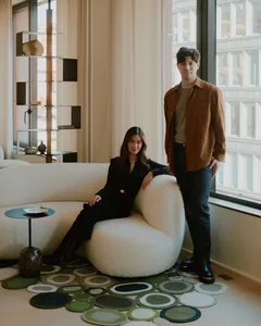 A modern living room featuring a round, white, wool-furniture sofa with a woman sitting on it and a man standing beside her, 
