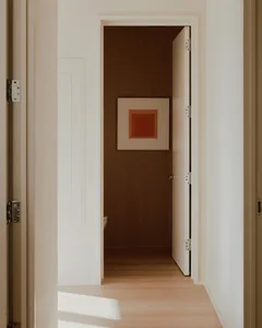 Modern minimalist bathroom featuring white walls and a wooden door with an abstract painting.