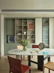 A modern minimalist residential interior with a round dining table, leather chairs, and a green plant on the table.