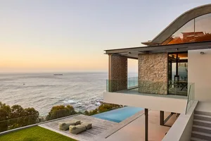 Modern residential exterior featuring a concrete, glass, and stone house with stunning ocean views and a pool.
