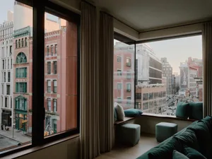 Modern living room with cityscape view through large windows, featuring soft textiles and upholstered seating