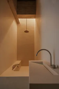 Modern minimalist bathroom with concrete walls and floor, featuring a sleek sink and bathtub with simple fixtures.