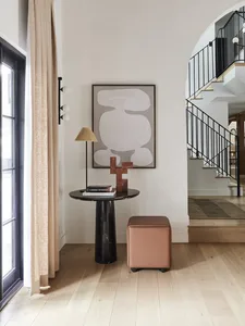 A minimalist entryway with a black marble pedestal table, a pink leather cube ottoman on wheels, and a modern light fixture w