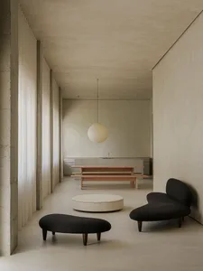 A modern living room with concrete walls, minimalist furniture, and a round ottoman.