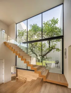 A modern interior design with wood, glass, and concrete, featuring a staircase with glass railings and a large window overloo