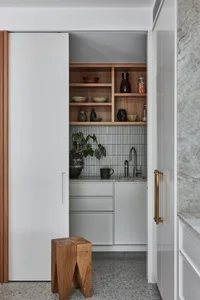 A modern kitchen with a white sliding door, wooden shelves, and a small wooden stool.