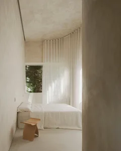 Minimalist bedroom with white curtains, window, and wooden stool