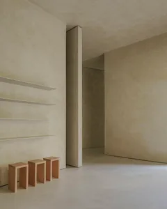 A modern minimalist interior with concrete walls and floors, featuring simple furniture and clean lines.