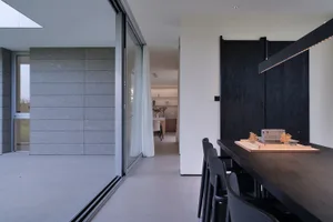 Modern minimalist dining room with black wood furniture and large windows.