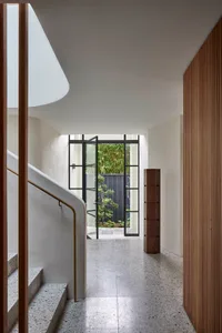 Modern minimalist entrance hall featuring a concrete staircase, glass door, wood accents, and a view of green foliage outside