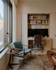 A modern minimalist home office with a blue armchair, desk, and built-in shelves.
